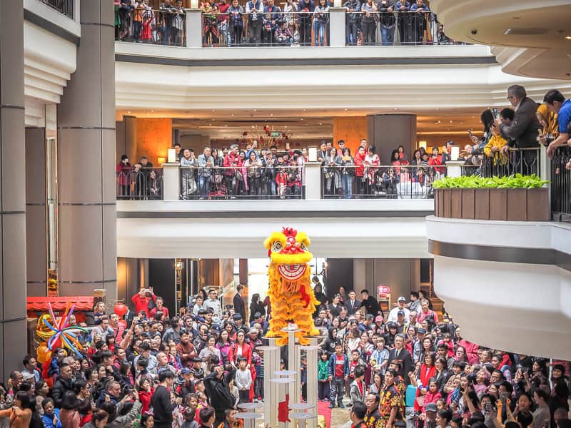 Crowds of people on several levels in a large lobby looking down on performers doing a lion dance
