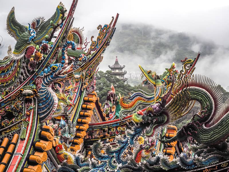 Looking out at a collection of temple rooftops, with a shrine on a misty mountain beyond