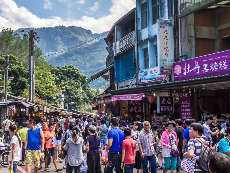 A crowded Neiwan Old Street with mountains behind