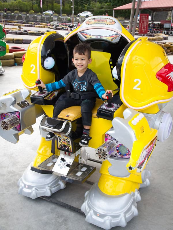 A young boy sitting on a large yellow robot and controlling it with two joysticks