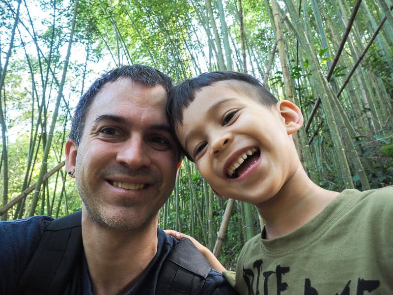 Close up shot of Nick Kembel and his young son as they put their heads together in a bamboo forest
