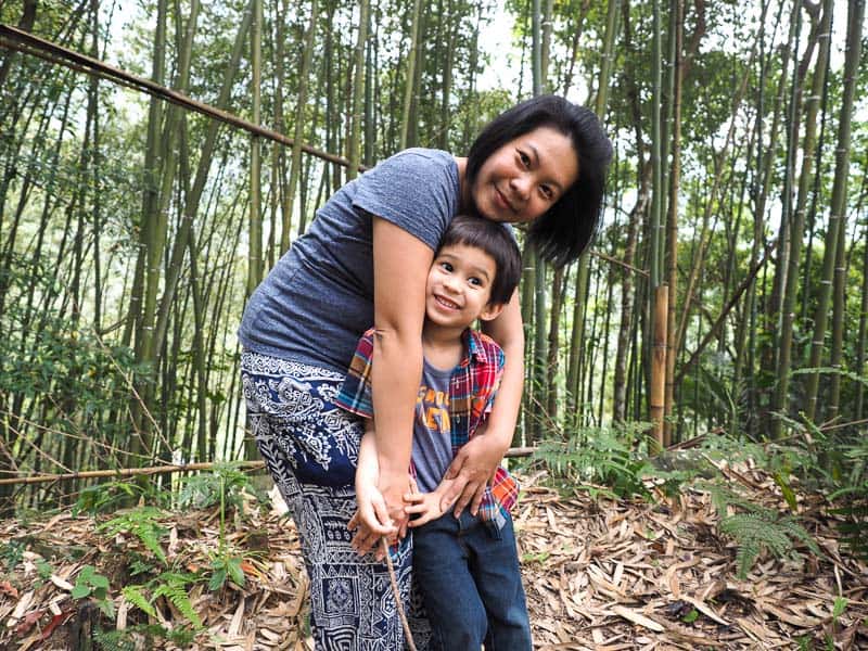 Nick's wife Emily bending and holding her son as they pose in a bamboo forest