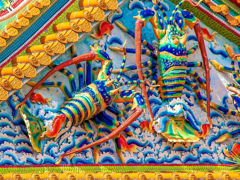 Close up of the colorful side of a temple's roof, with two huge lobster statues sticking out