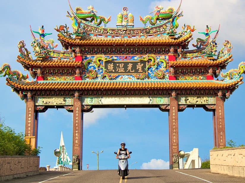 Nick Kembel riding a scooter through a large Taiwanese-style traditional gate over the road on the Penghu Islands in Taiwan