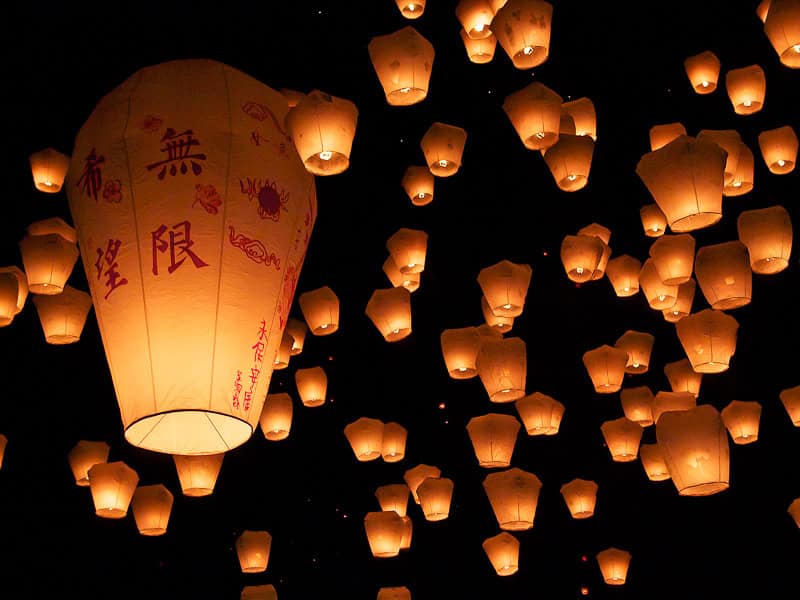 A black sky filled with sky lanterns, including one especially big one