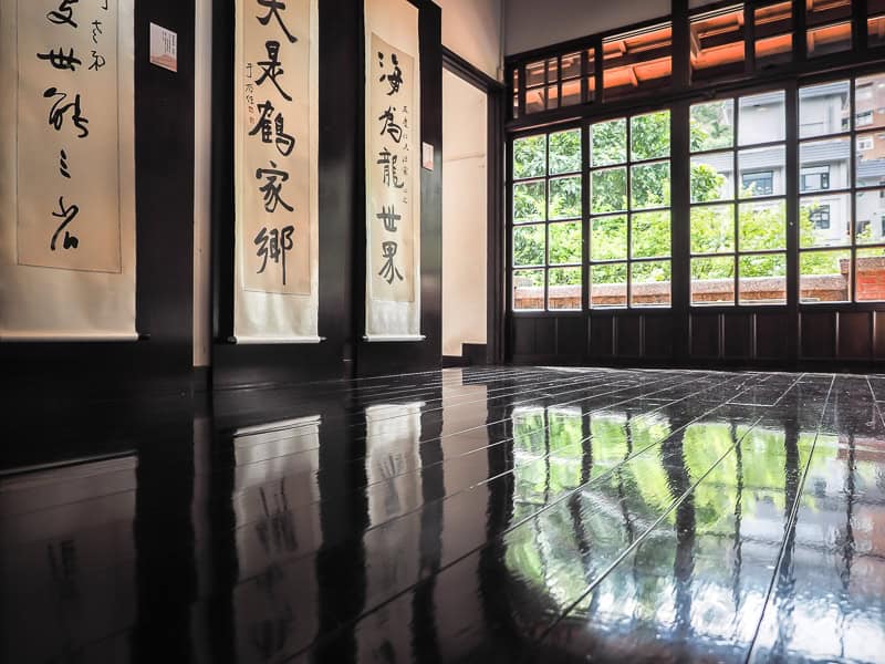 The interior of a black wooden Japanese style room with posters of characters hanging on the walls and windows looking out to trees