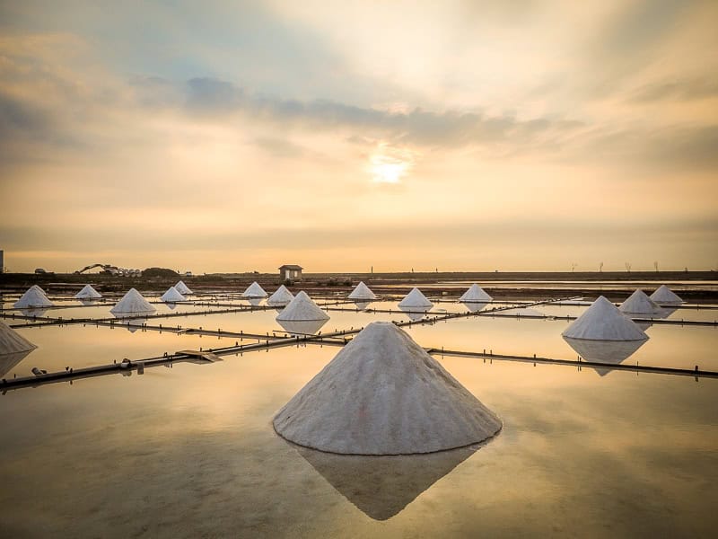 A field of flooded salt flats, with pyramidal mounds of salt in each one, shot at sunset