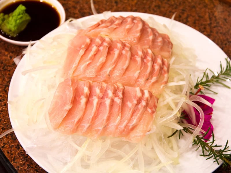 A plate of pink sashimi on top of onion slices, with a small dish of soy sauce and wasabi on the side