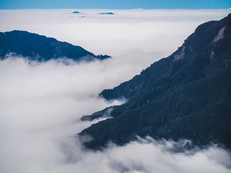 A couple mountain peaks poke out from a dense sea of clouds