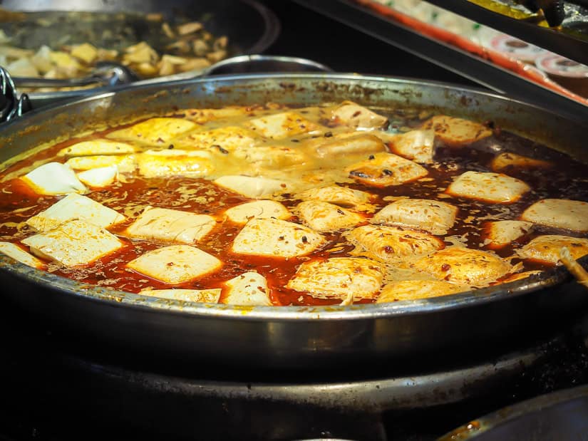 A large metal vat of spicy soup with blocks of stinky tofu floating in it
