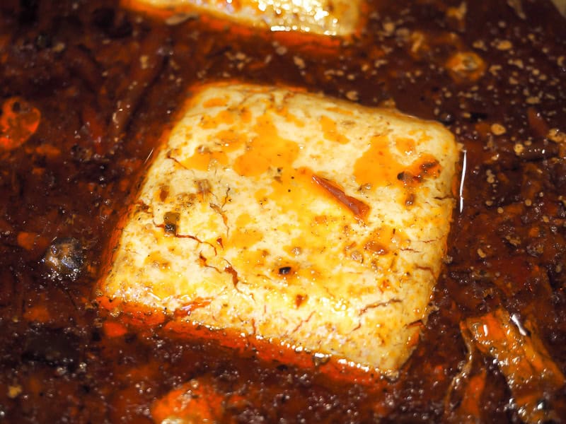 Close-up of a square of tofu floating in a spicy broth
