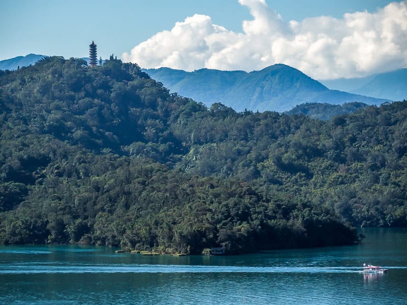 A lake with forest hills beyond, and a pagoda at the top of one of them