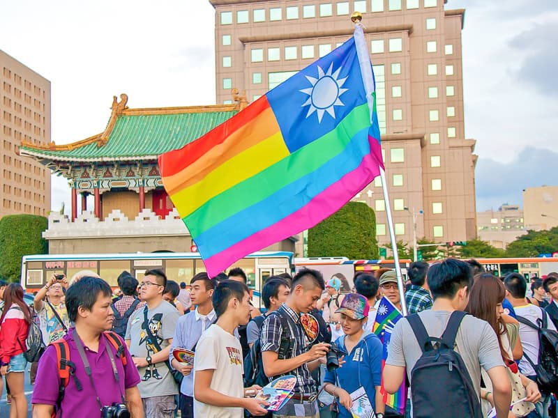 A group of people at a Pride gathering in Taipei, with a Taiwanese flag but in rainbow colors