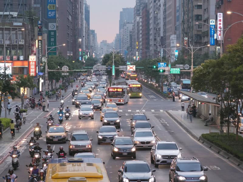 Looking up a large main street in Taipei, with a bus, several cars, and several scooters driving towards the camera