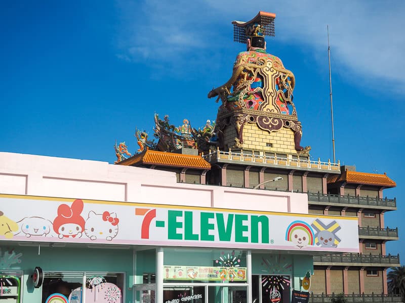 A cute 711 storefront, with the back of a huge Taoist statue on a temple behind it