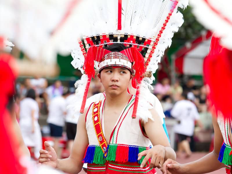 A Taiwanese aboriginal young man in traditional costume dancing while holding the hands of other performers on either side of him