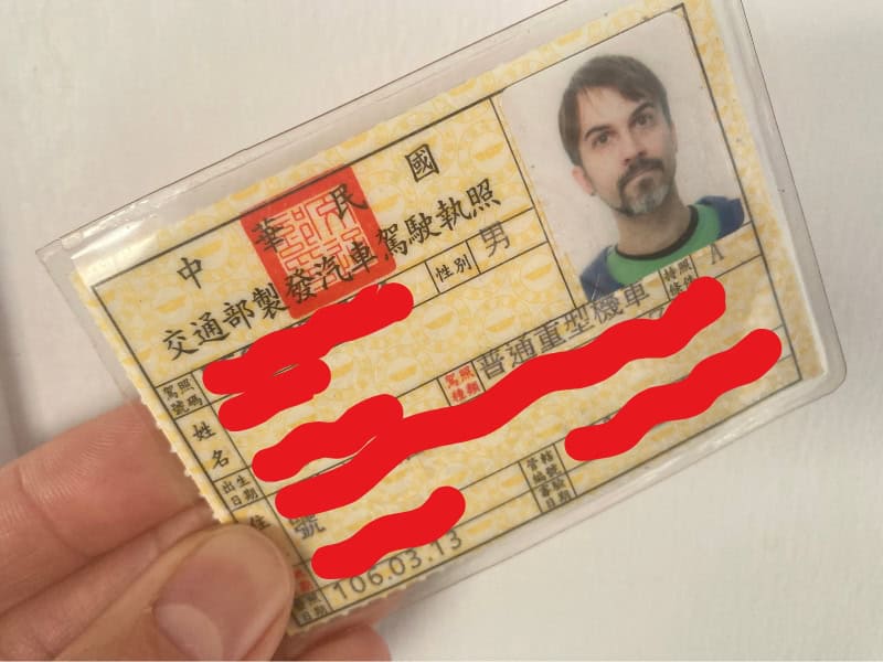 Close up of a hand holding a Taiwanese scooter license, with all the personal data hidden behind squiggly red lines