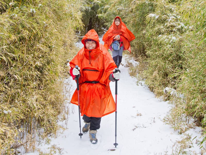 An elderly Taiwanese couple hiking on a snowy trail wearing orange rain ponchos