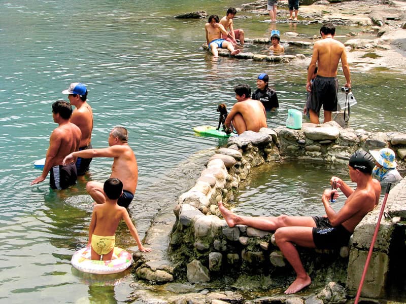Some Taiwanese people bathing in small hot spring pools at the side of a river in Wulai