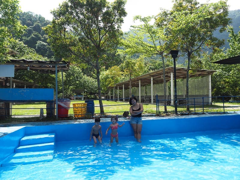 A mother and two kids standing in shallow water in a blue pool in a campground
