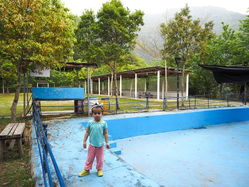 A young girl standing beside an empty swimming pool in a campground