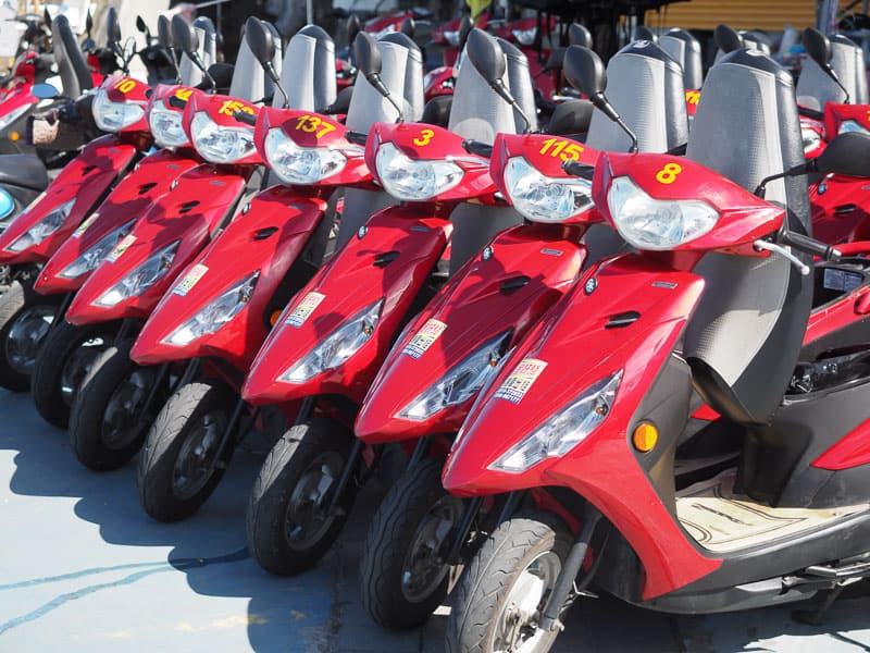 A row of 8 parked red scooters, each with a yellow number on the front