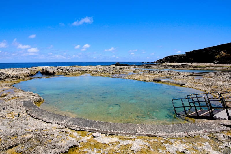 A round thermal hot spring pool beside the sea with coral bottom
