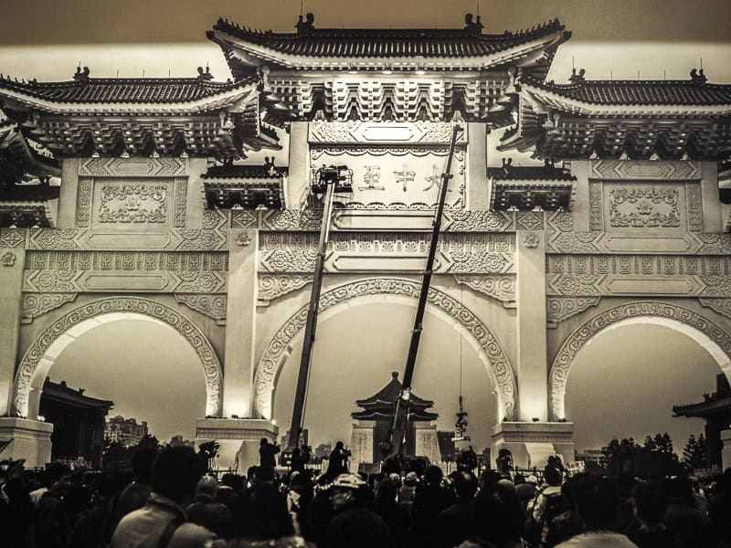 Black and white photograph of a crowd of people at Liberty Arch in CKS Memorial hall, with long poles removing the Mandarin characters from the arch