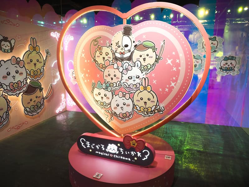 A large, spinning, heart shaped display with Chiikawa anime characters inside it and colorful walls behind