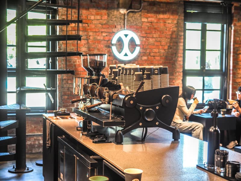 A large espresso machine on the counter inside a cafe with red brick wall behind