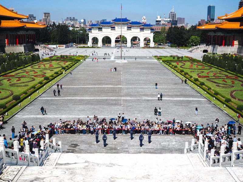 Looking down a white staircase at a guard changing ceremony on Liberty Square below and Liberty Arch in the distance