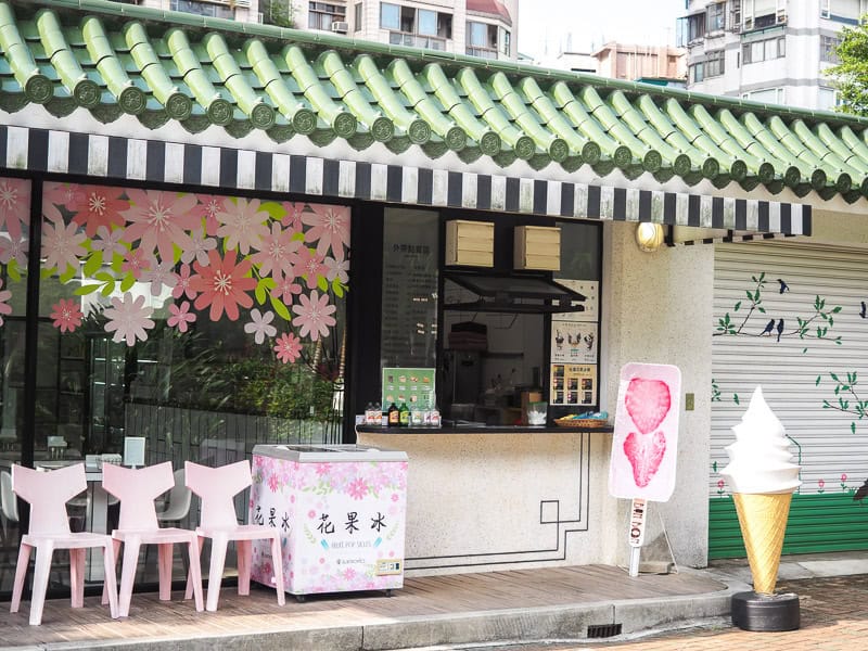 Front of a small cafe with some chairs outside and signs with ice cream and flowers