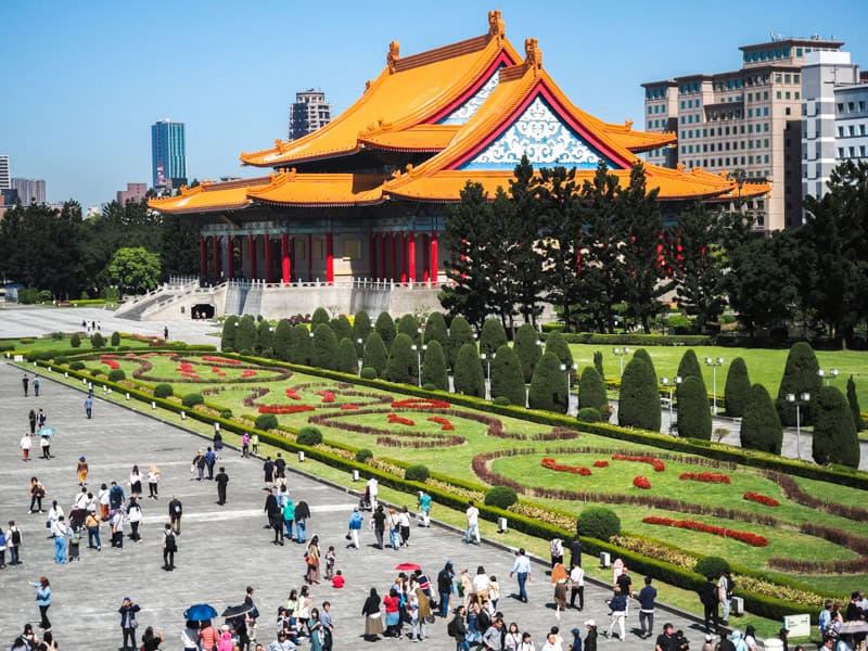 Crowds of people walking on a cement walkway called with manicured lawns on the side and National Concert Hall behind