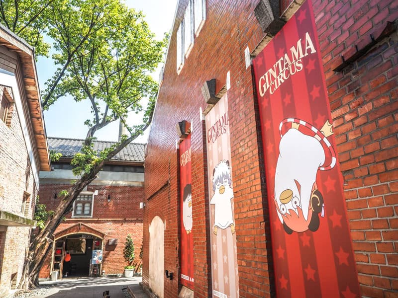 The exterior of a red brick building with some banners on the side advertising a Gintama Circus cartoon pop-up