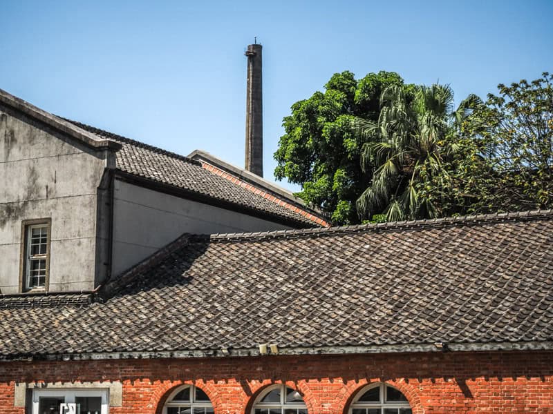 A red brick building, connecting cement building, plus trees and a cement smokestack behind, at Huashan 1914 Creative Park in Taipei