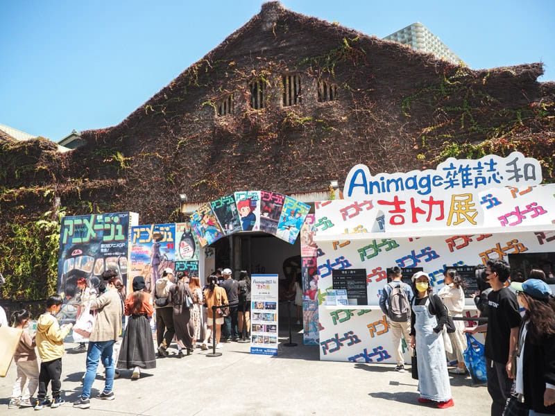 An old warehouse covered in vines at Huashan, with many signs advertising a Animage anime pop-up event inside and some people lined up to go in