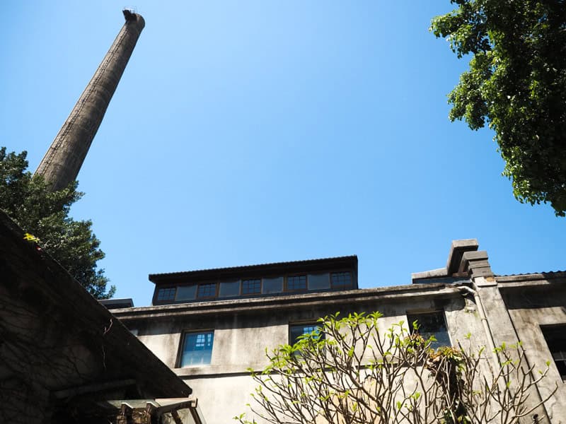 The top of a cement factory building with tall smokestack rising into the blue sky from the left side