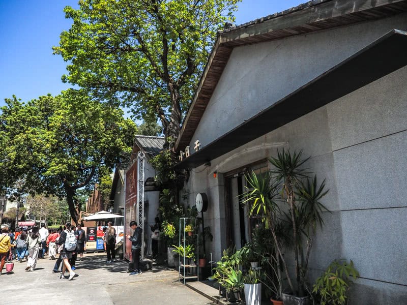 An old garage warehouse containing a gift shop, with trees and some pedestrians behind