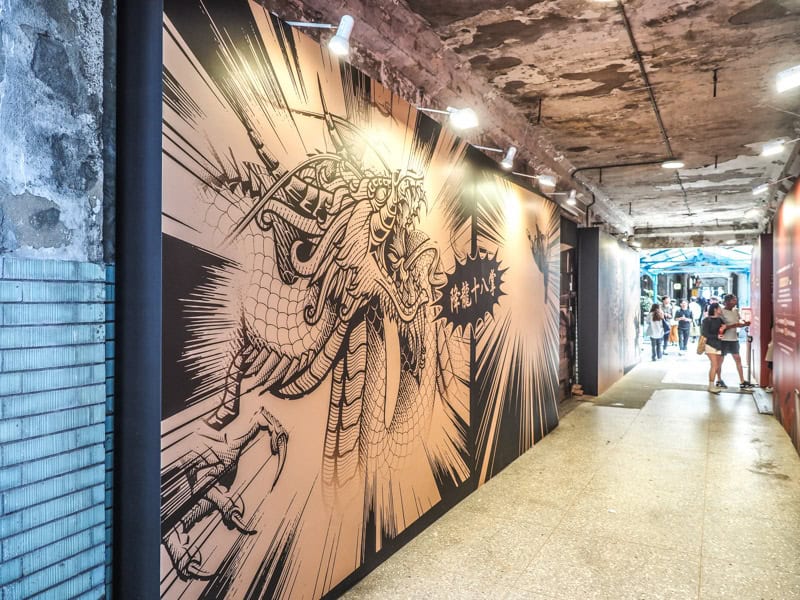 Looking down a hallway with a dragon mural painted on one side and some people further down