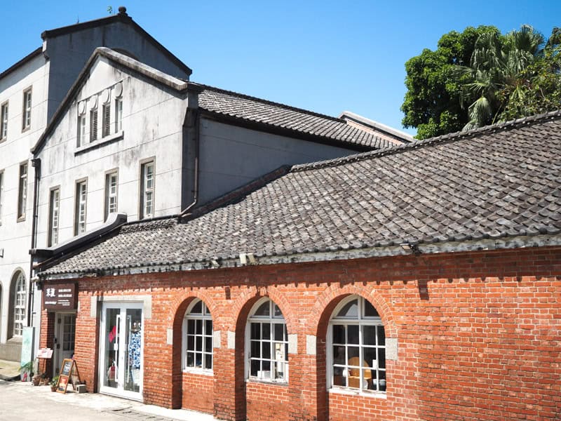 Three connected buildings – two cement ones on the left and a lower red brick one on the right