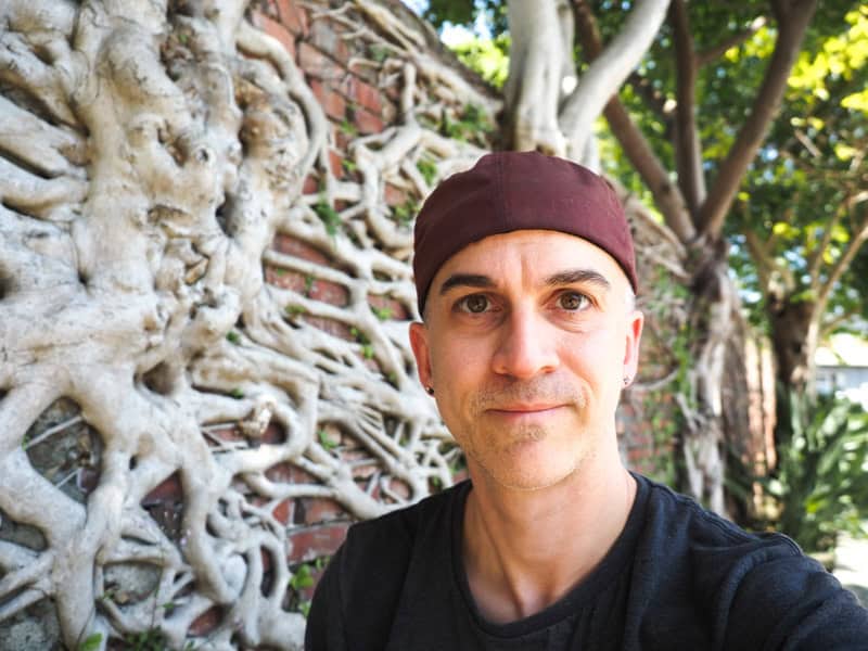 Nick Kembel posing in front of a brick wall covered in banyan tree roots