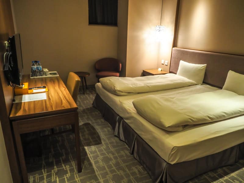 Inside a dimly lit hotel room with double bed and desk