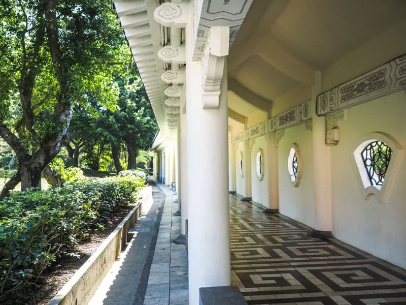 Looking down a long covered roofed corridor with white columns and open to trees on one side