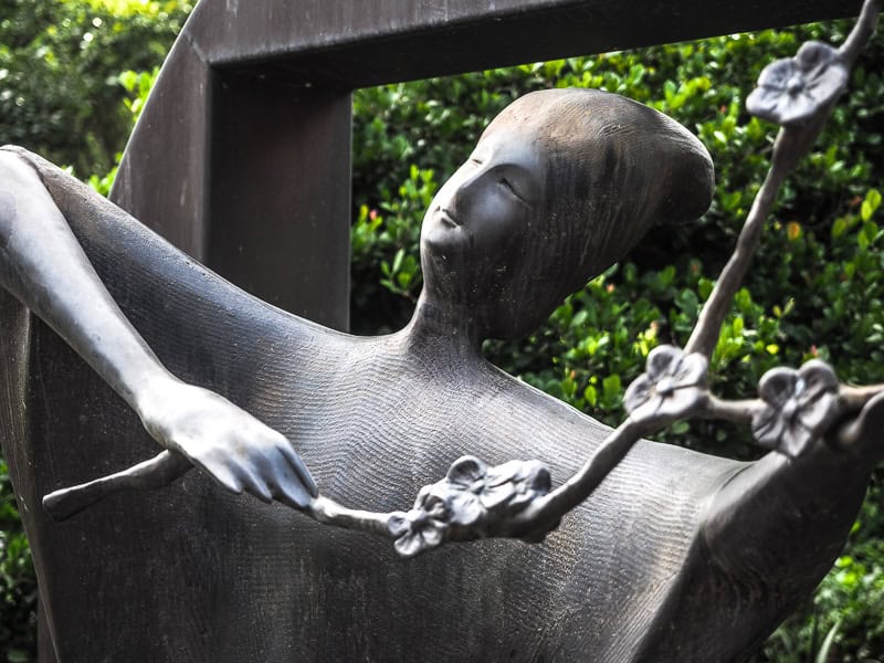 A artistic statue of a woman holding up a vine with flowers
