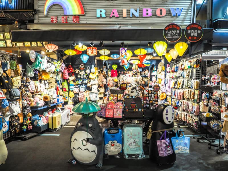 A shop in a night market with open front and statues of Totoro and No Face