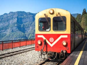 Yellow and red Alishan Forest Railway car parked at Erwanping station on the way to Alishan, with Tashan Mountain visible behind