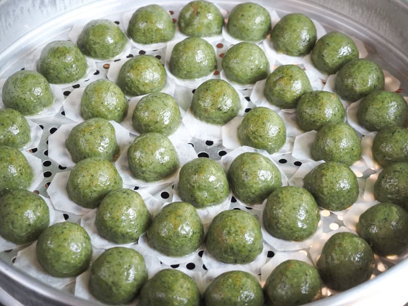 A large, round, metal steaming rack filled with green steamed dumplings 