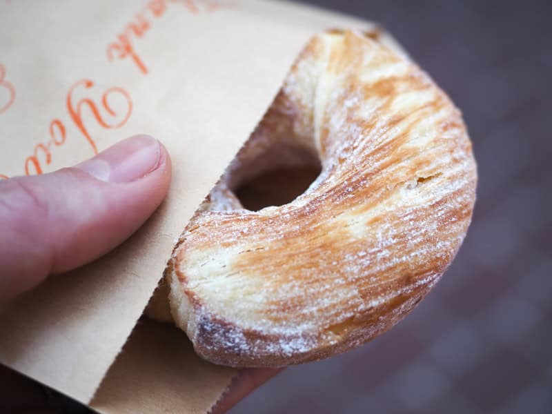 A hand holding a donut sticking out of a paper bag