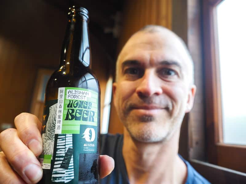 Nick Kembel with shaved head, holding up a bottle of Alishan Forest Railway honey beer