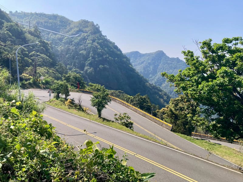 Looking down at a series of switchbacks, with mountains in the distance and Taiping Suspension Bridge visible at the top-left